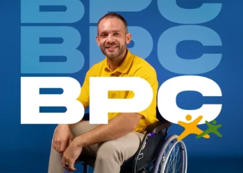 Homem em cadeira de rodas com camisa amarela, sorrindo, representando inclusão social com o logo BPC ao fundo.