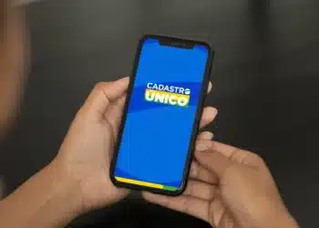 Imagem de uma pessoa segurando um smartphone com o aplicativo Cadastro Único aberto, mostrando a tela de login.