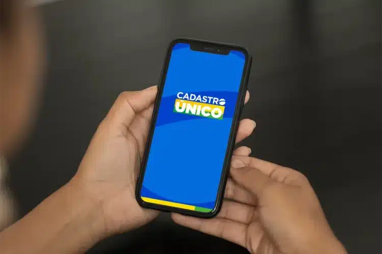 Imagem de uma pessoa segurando um smartphone com o aplicativo Cadastro Único aberto, mostrando a tela de login.