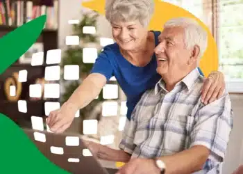 Casal de idosos sorrindo enquanto usam um laptop juntos em casa.
