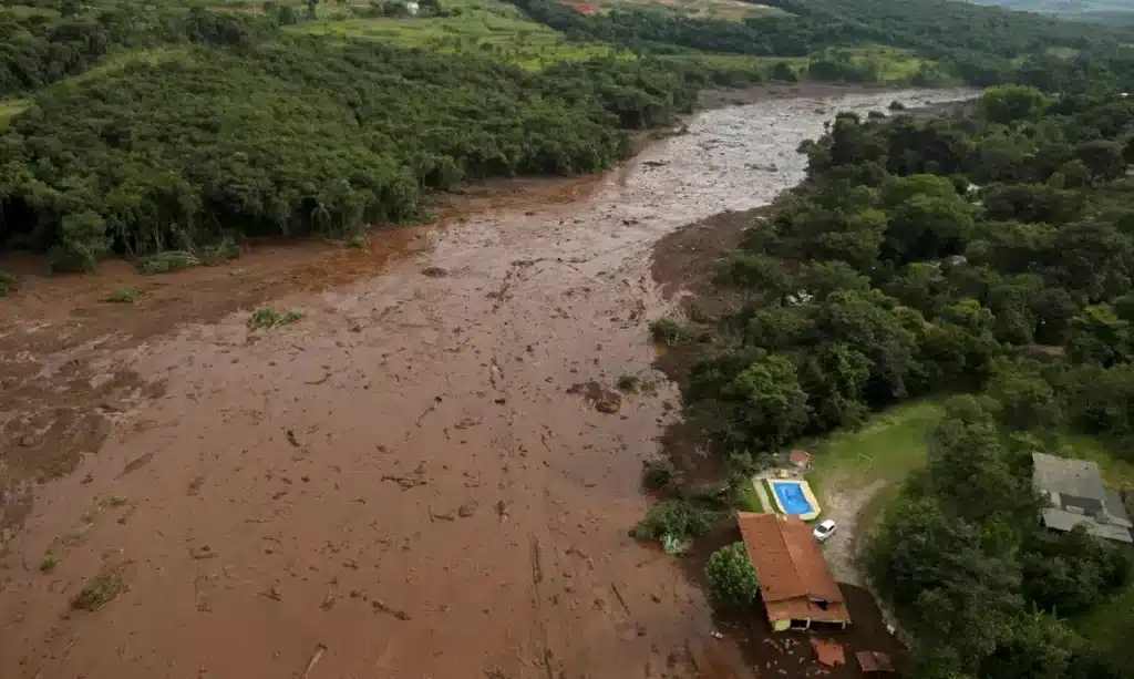 Imagem aérea mostrando uma grande área afetada por um desastre ambiental, com lama cobrindo parte da vegetação e estruturas. Imagem aérea mostrando uma grande área afetada por um desastre ambiental, com lama cobrindo parte da vegetação e estruturas.