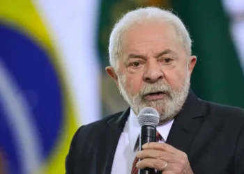 Lula discursando em evento com bandeira do Brasil ao fundo.