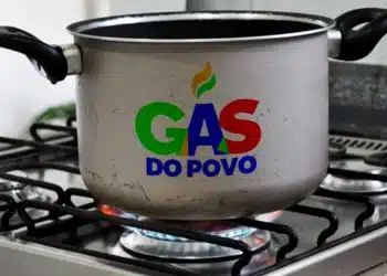 Gás do Povo: 15 milhões de lares poderão recarregar o gás de cozinha de graça até março 10 Panela com logo Gás do Povo aquece no fogão aceso em cozinha residencial.