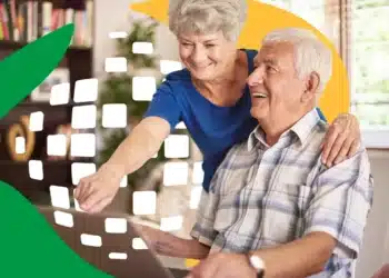 Aposentados poderão comparar ofertas e escolher a melhor taxa no novo leilão do INSS 10 Mulher sorrindo aponta para tela de notebook ao lado de homem idoso sentado na sala