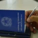 Seguro-Desemprego muda em 2026; veja detalhes do novo cálculo 11 Mão segurando caneta preenche carteira de trabalho azul sobre mesa clara