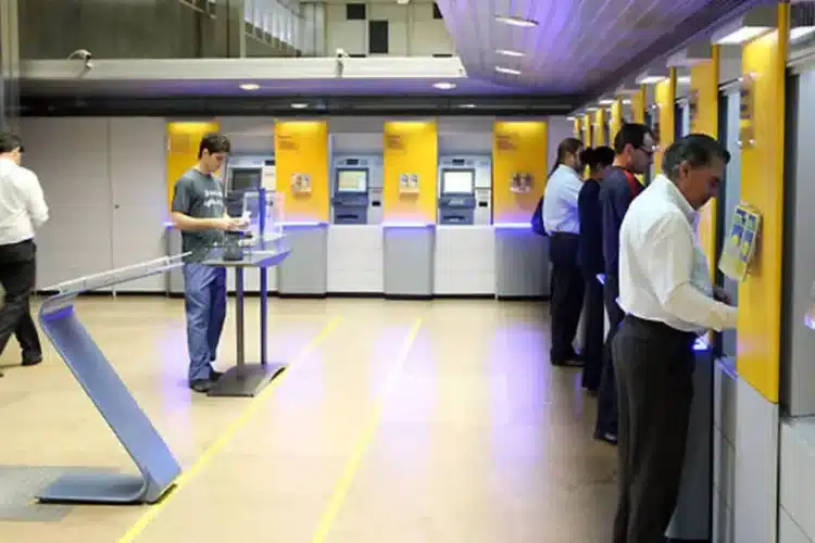 Agencias bancárias fechadas no feriado 2026 Pessoas usando caixas eletrônicos em agência bancária iluminada
