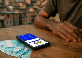 Celular com aplicativo do Bolsa Família aberto ao lado de notas de R$ 100, ilustrando consulta de março no app.