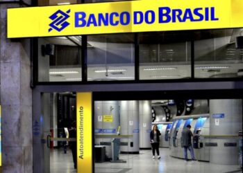 Pessoas utilizando caixas eletrônicos em agência do Banco do Brasil iluminada à noite