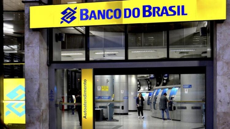 Pessoas utilizando caixas eletrônicos em agência do Banco do Brasil iluminada à noite