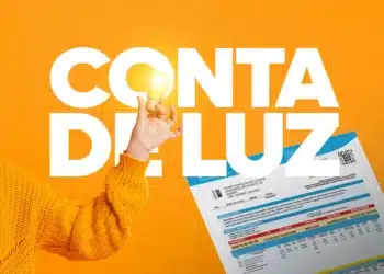 Conta de luz pode cair ou zerar? Governo envia mensagens e revela quem tem direito 7 Mão com blusa laranja segura lâmpada acesa ao lado de fatura de energia sobre fundo amarelo.