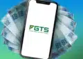 Saque-aniversário do FGTS é liberado nesta segunda-feira (4); descubra se você tem direito 15 Celular com logotipo do FGTS sobre leque de notas de R$ 100, representando o valor liberado pelo saque-aniversário aos aniversariantes de maio em 2026