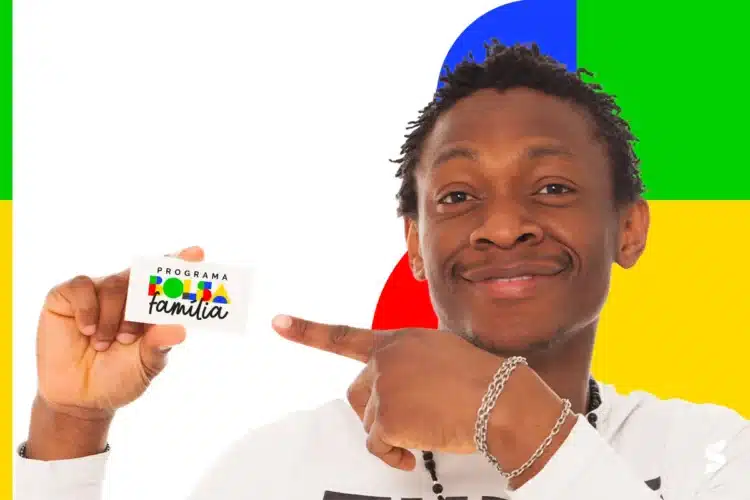 Bolsa Família 2026 Homem sorrindo, segura cartão do Bolsa Família e aponta para ele em frente a fundo com blocos amarelo, verde, vermelho e azul