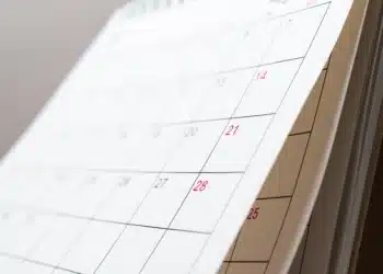 Próximo feriado pode garantir folga prolongada; confira o calendário de 2026 6 Calendário de papel com dias em vermelho destacando fins de semana, apoiado sobre base marrom.