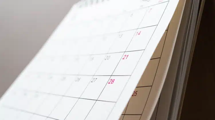 Próximo feriado pode garantir folga prolongada; confira o calendário de 2026 1 Calendário de papel com dias em vermelho destacando fins de semana, apoiado sobre base marrom.
