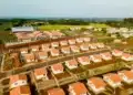 Reforma Casa Brasil vs. Minha Casa Minha Vida: qual é o ideal para você? 3 Vista aérea de conjunto habitacional com casas brancas padronizadas e telhados laranjas em área rural verde.