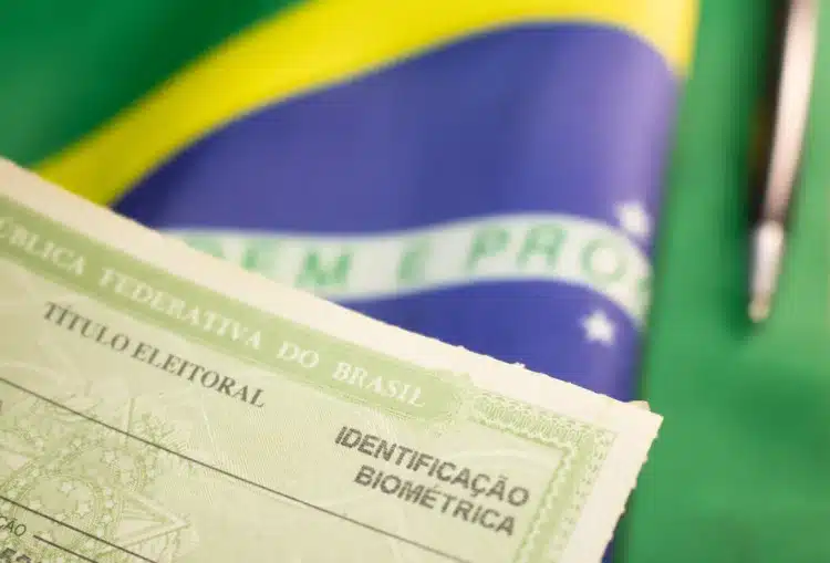 Situação eleitoral: como saber se seu título está apto para votar em 2026 1 Título eleitoral da República Federativa do Brasil com identificação biométrica em primeiro plano e bandeira brasileira ao fundo.