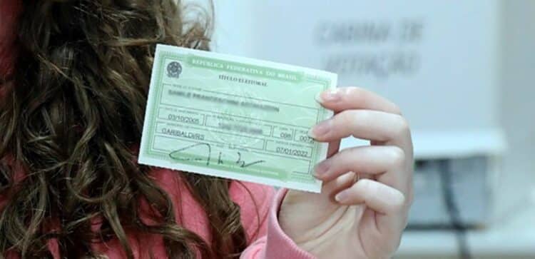 Mulher de cabelos castanhos cacheados segura título eleitoral verde da República Federativa do Brasil.