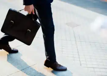 O que diz a CLT sobre trabalhar no feriado de Tiradentes 6 Pessoa de terno azul-marinho com pasta executiva de couro marrom e sapatos sociais caminha em calçamento.