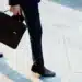 O que diz a CLT sobre trabalhar no feriado de Tiradentes 12 Pessoa de terno azul-marinho com pasta executiva de couro marrom e sapatos sociais caminha em calçamento.