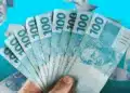 Bolsa Família e BPC terão pagamento unificado em municípios em emergência 12 Pessoa segurando notas de cem reais