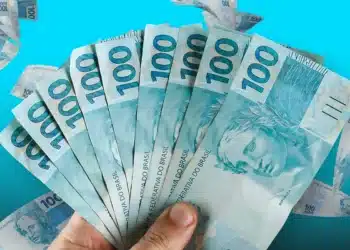 Bolsa Família e BPC terão pagamento unificado em municípios em emergência 7 Pessoa segurando notas de cem reais