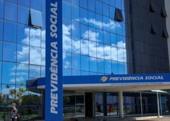 Fachada de vidro azul do edifício-sede da Previdência Social, com o letreiro do INSS na entrada
