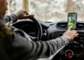 Motorista ao volante toca a tela de um celular com aplicativo de mapa