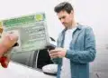 Nova CNH: aluno agora pode escolher instrutores e autoescolas pelo app 12 Homem utilizando celular ao lado de carteira de habilitação