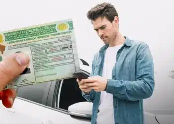 Nova CNH: aluno agora pode escolher instrutores e autoescolas pelo app 5 Homem utilizando celular ao lado de carteira de habilitação