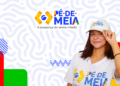 Estudante de boné e camiseta do Pé-de-Meia sorri ao lado da logomarca do programa