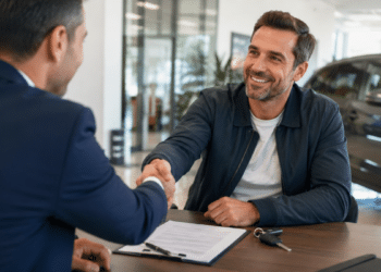Dois homens se cumprimentam sorrindo em escritório com chaves e contrato sobre a mesa
