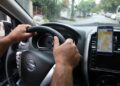 Mãos de motorista em volante de Nissan com aplicativo de corrida exibido no celular no painel