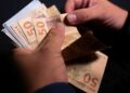 Trabalhador conta notas de cinquenta reais recebidas do benefício