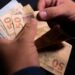 Trabalhador conta notas de cinquenta reais recebidas do benefício