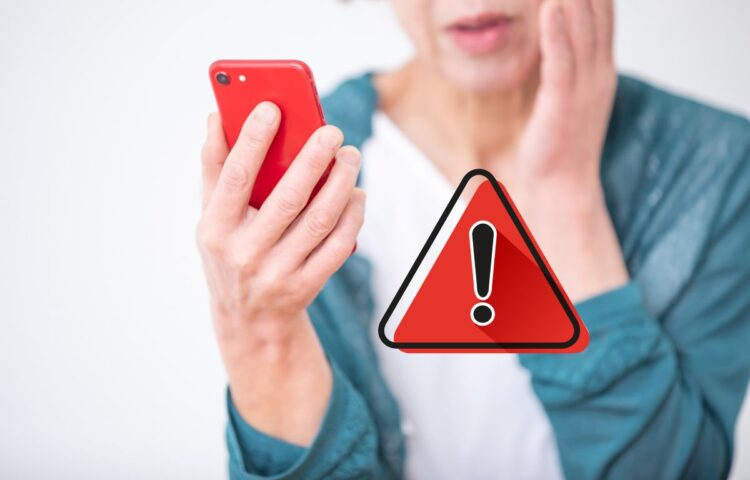 Mulher preocupada olha o celular ao lado de ícone vermelho de aviso