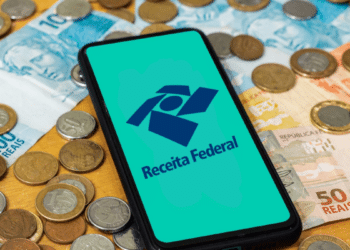 Logo da Receita Federal exibida em celular com cédulas e moedas ao fundo.