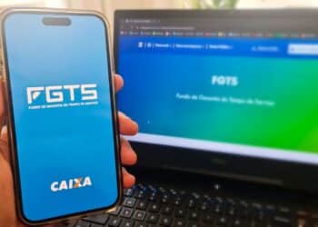 Tela do app FGTS da Caixa aberta em celular à frente de notebook com site do FGTS, foco em azul