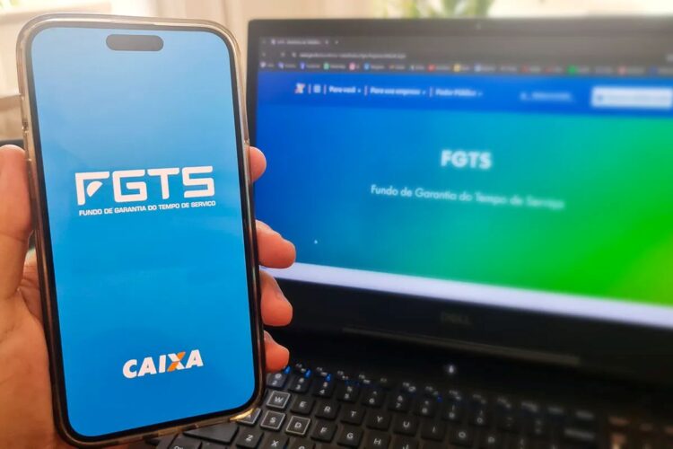Tela do app FGTS da Caixa aberta em celular à frente de notebook com site do FGTS, foco em azul